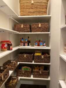 2 lazy susans with sauces on a shelf along with brown woven storage baskets on the lower 2 shelves and upper two shelves..