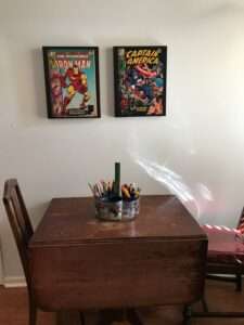 A table with the pencil and marker container, under some comics framed on the wall.