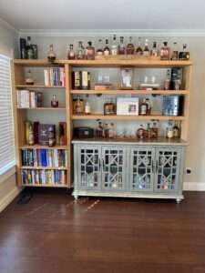 Well organized whisky bar with books on the viewers left side, and most of the whisky on the right.