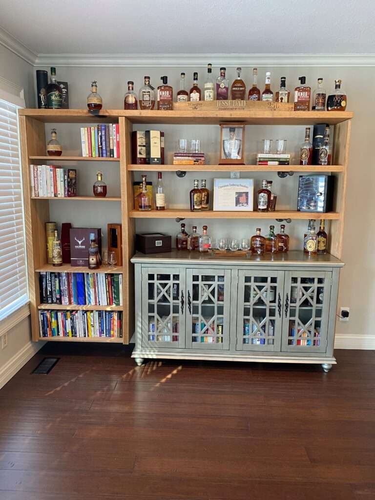 Well organized whisky bar with books on the viewers left side, and most of the whisky on the right.