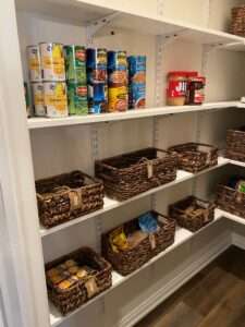 Canned goods on a shelf along with brown woven storage baskets on the lower 2 shelves.