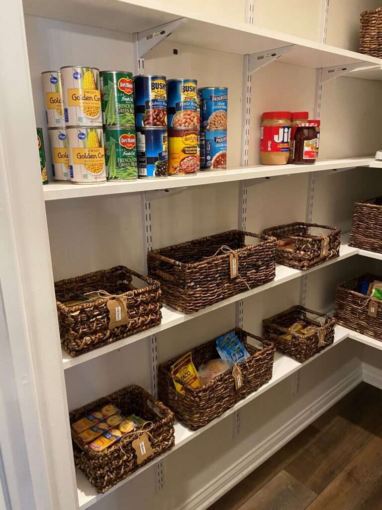 Canned goods on a shelf along with brown woven storage baskets on the lower 2 shelves.