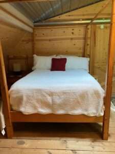 A large bed with a white duvet, white pillow cases and a red accent pillow in the middle. The walls are rustic, unfinished wood.
