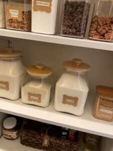 Dry goods, brown sugar, sugar, flour, etc, are stored in some glass and plastic containers in this kitchen pantry organization.