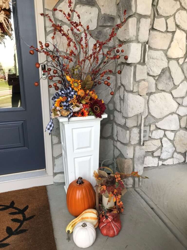 An outdoor fall arrangement on a porch with pumpkins and leaves.
