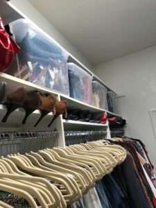 More shoe storage on the middle row, with plastic organizing bins on the top row, and pants and shirts on hangers on the bottom row of the closet shelves.