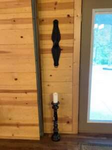 A candle on a rustic stand and a wallhanging.