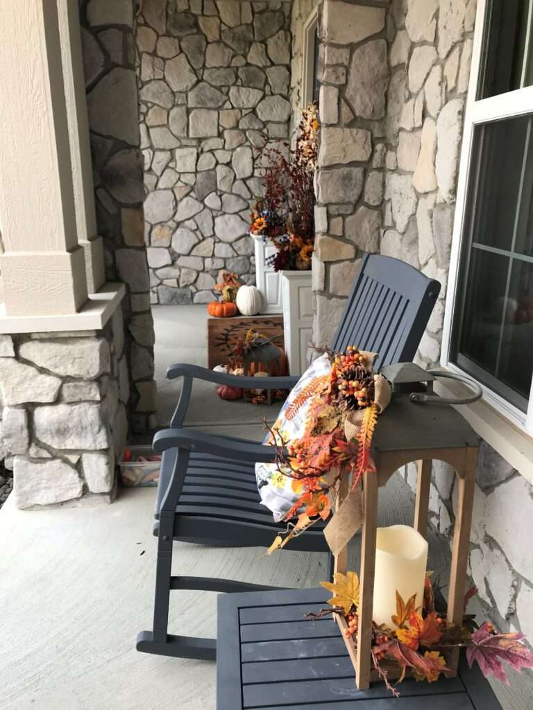 An outdoor fall arrangement on a porch with pumpkins and leaves.
