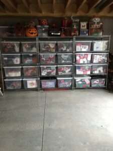 3 tall metal shelves in a garage, filled with totes of organized holiday decorations.