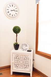 Small white cabinet with plant and décor on top, under a white clock.