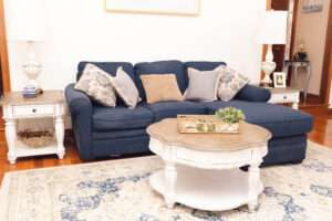 The blue couch in the background, and in front is a circular white table with natural decorations sitting on a white rug with blue patterning.