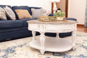 The blue couch in the background, and in front is a circular white table with natural decorations sitting on a white rug with blue patterning.