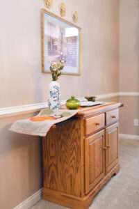 A side table with a blue and white floral vase, a small green glass dish, and white serving tray with white pear handles. There is a fall pumpkin themed runner and the table is extended for serving.