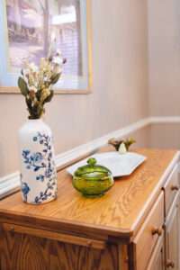 A side table with a blue and white floral vase, a small green glass dish, and white serving tray with white pear handles.