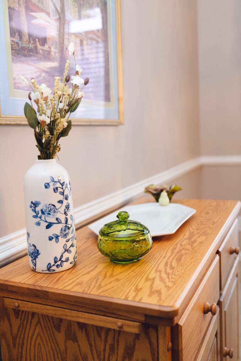 A side table with a blue and white floral vase, a small green glass dish, and white serving tray with white pear handles.