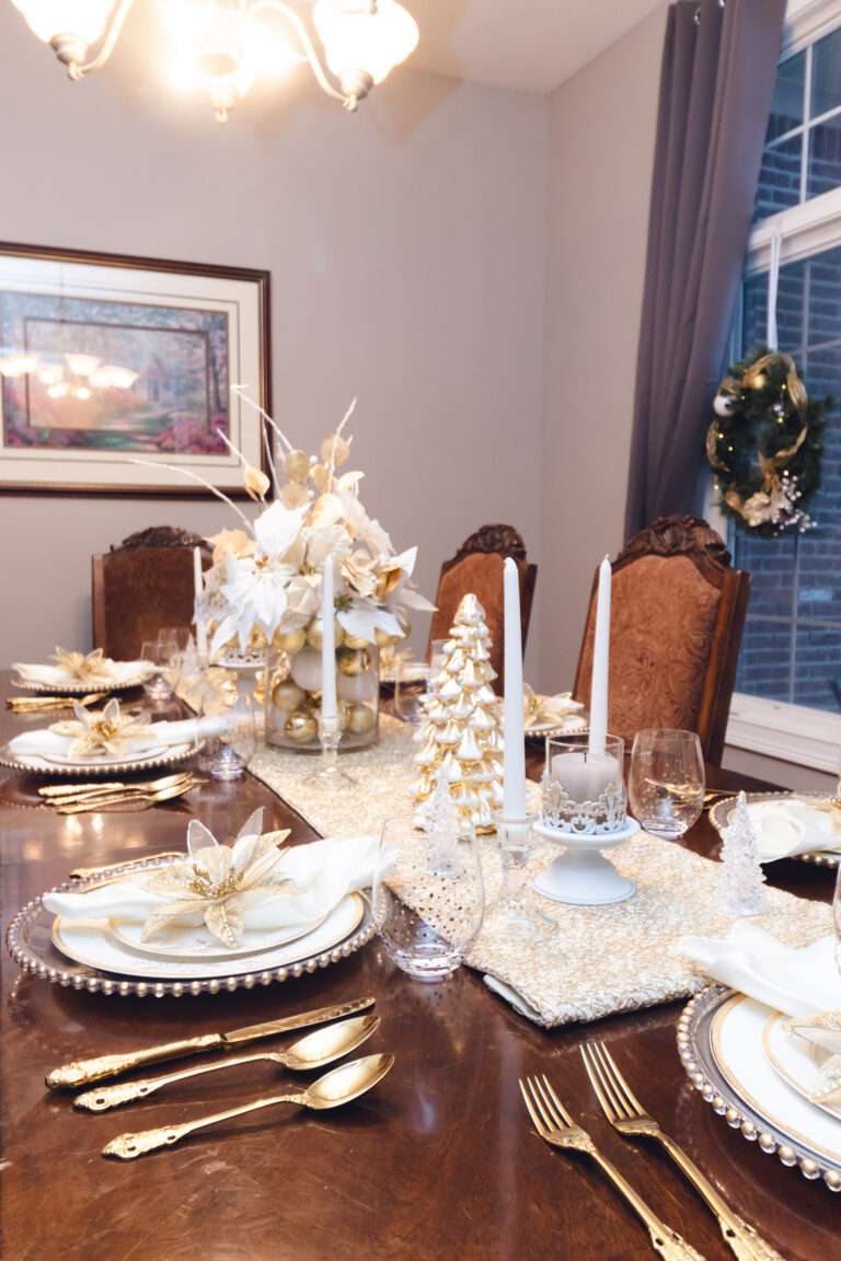 Gold and white Christmas tablescape, with white runner, white and gold Christmas tree, and floral arrangement with white and gold ornaments over a rich brown wooden table.