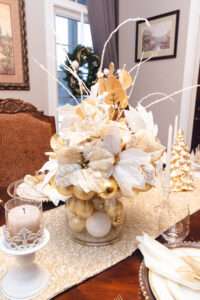 Close up of a floral arrangement with white and gold ornaments over a rich brown wooden table.