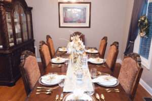 Gold and white Christmas tablescape, with white runner, white and gold Christmas tree, and floral arrangement with white and gold ornaments over a rich brown wooden table.