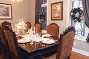 Gold and white Christmas tablescape, with white runner, white and gold Christmas tree, and floral arrangement with white and gold ornaments over a rich brown wooden table.