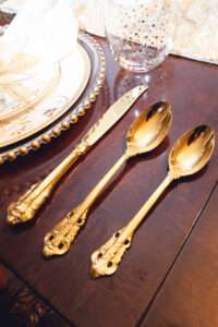 Close up of gold silverware next to a decorative place setting.