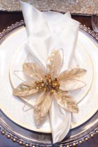 A napkin with a gold and white flower arranged on a white plate.