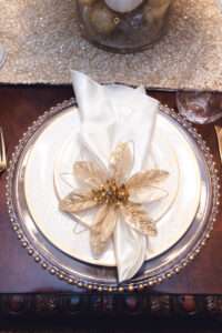 A napkin with a gold and white flower arranged on a white plate.