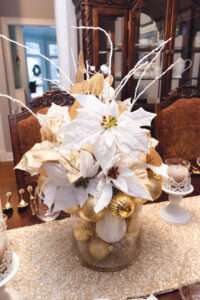 Close up of a floral arrangement with white and gold ornaments over a rich brown wooden table.