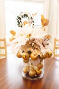 A white and gold floral arrangement in the center of a wooden table.