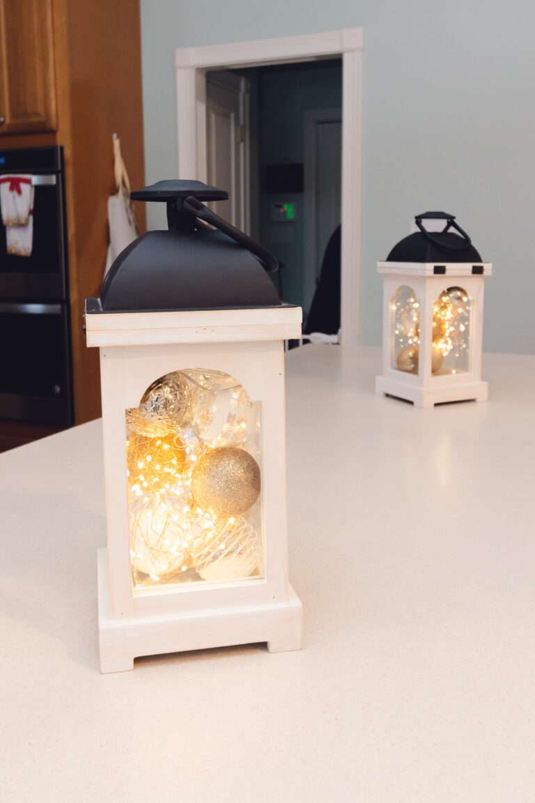 White lanterns with matte black handles, filled with white, gold, and clear ornaments with lights inside.