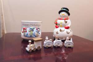 A table display with a Frosty the Snowman candle holder, additional snowmen decorations, and a white and gold ceramic train.